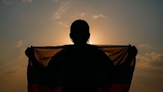 Standing silhouette holding flag at sunset with sun halo and dramatic backlight