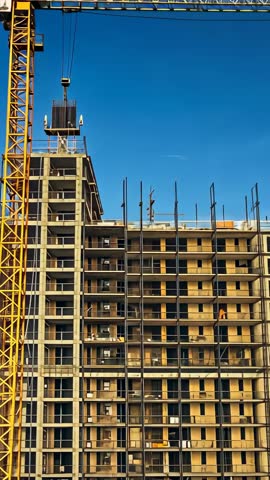 Vertical panning across high-rise construction, crane lifting container with rebar