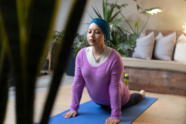 Relaxed biracial woman in hijab stretching in yoga pose on mat in living room, with copy space. Happiness, health, fitness, inclusivity and domestic life.