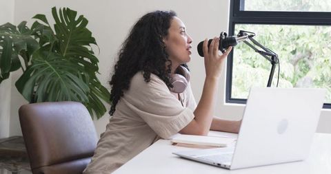 African american woman recording podcast at desk with microphone, laptop and headphones
