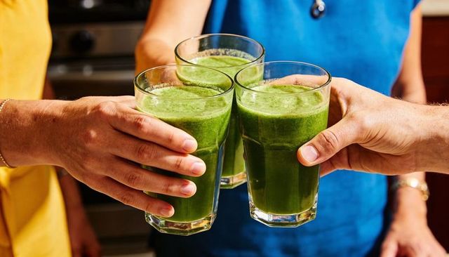 Three friends toasting green smoothies in kitchen for healthy morning cheer