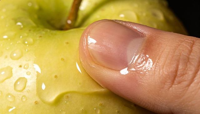Macro thumb pressing glossy green apple creating shallow dent and water trail