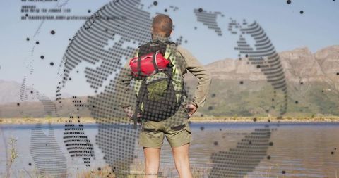 Backpacker standing overlooking lake and mountain peaks with red sleeping bag