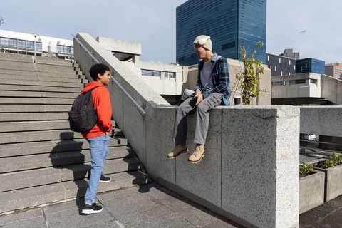 Urban friends chatting on plaza stairs with camera and coffee in city daylight
