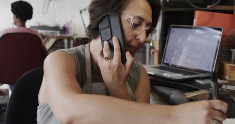 Jewellery designer communicating on smartphone in creative workshop