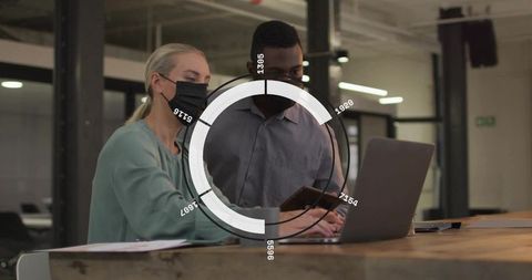 Masked colleagues collaborating on laptop and tablet in open-plan office with data overlay