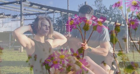 Couple Exercising Outdoors Among Daisies Doing Abdominal Crunches
