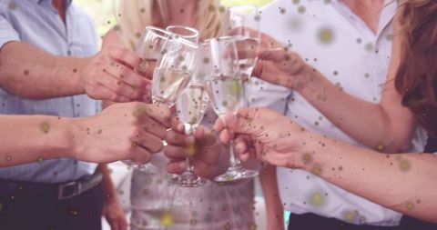 Friends clinking champagne flutes in daylight celebration with confetti, joyful toast