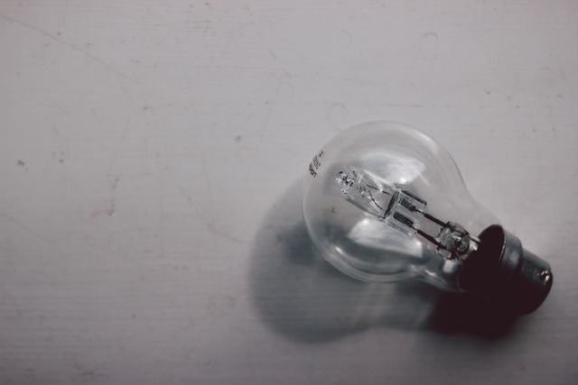 Single clear light bulb laying on white surface. Perfect for illustrations related to electricity, innovation, ideas, illumination, power sources, simplicity, and background elements for graphic design or promotional materials.