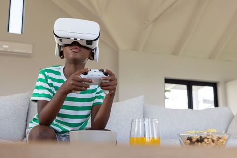 African American Boy Wearing VR Headset Holding Controller on Sofa in Modern Living Room