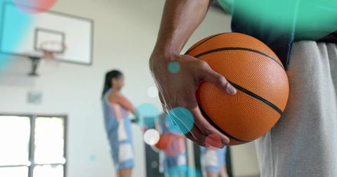 Holding basketball at hip with blurred teammates on indoor court training session