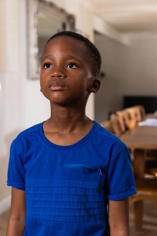 Thoughtful african american boy looking up in dining room wearing cobalt t-shirt