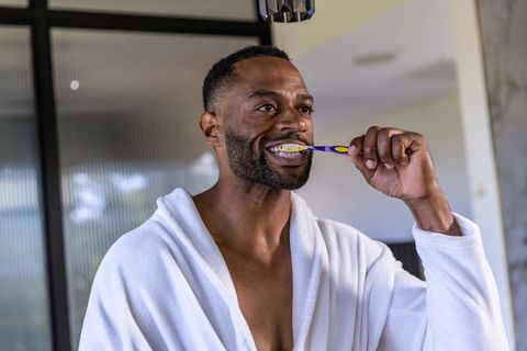 Man wearing white bathrobe brushing teeth in modern bathroom morning grooming routine