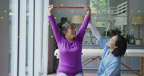 Asian woman stretching with resistance band while receiving guided physiotherapy at home