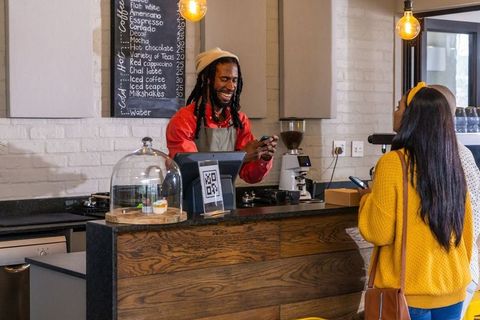 Smiling barista processing mobile payment with qr code at cozy urban coffee counter