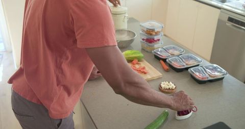 Mature man preparing meal prep on kitchen island with containers and fresh vegetables