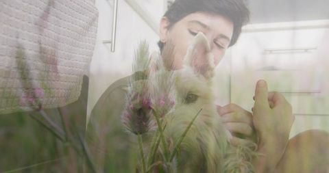 Woman cradling small fluffy dog on bedroom floor double exposure wildflowers calm