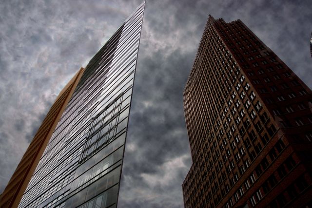 Modern skyscrapers with glass facades reach towards a dramatic, cloudy sky. Perfect for visual pieces focusing on urban architecture, city life, and the intersection of modern design with nature. Suitable for blogs, presentations, or editorials about urban development, real estate, or city planning.