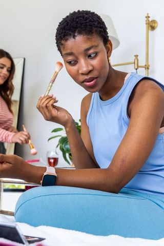 Multiracial friends applying makeup together in cozy bedroom beauty routine