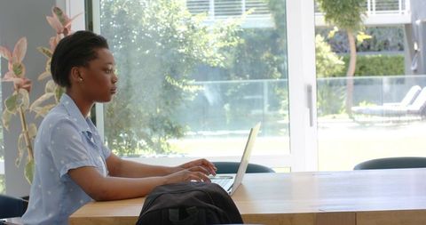 Young african woman working remotely on laptop at minimalist table with garden view