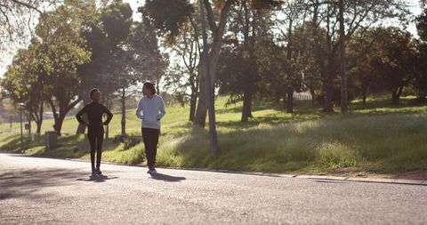 Diverse friends walking and chatting on sunlit park path in workout clothes