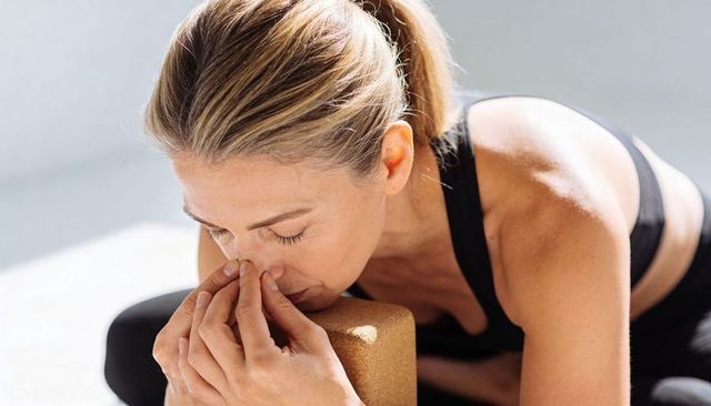 Woman practicing restorative yoga breathing, pinching nose with cork block in sunlit studio