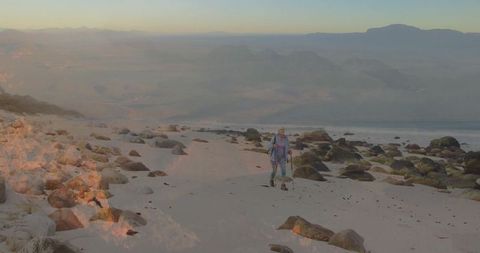 Woman hiking along secluded rocky beach offers opportunity to highlight themes of exploration, adventure, and peace in nature. Ideal for promoting travel, outdoor activities, or features about experiencing remote natural settings.