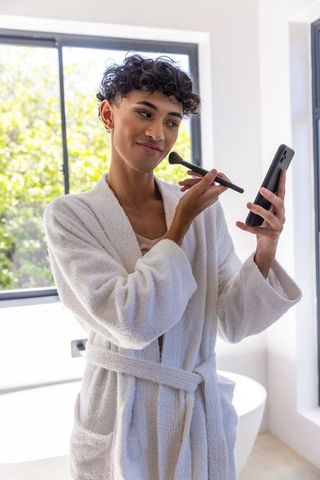 Man in Bathrobe Applying Makeup with Smartphone Guidance