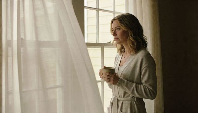 Woman holding ceramic mug and looking out window in cozy belted robe reflection