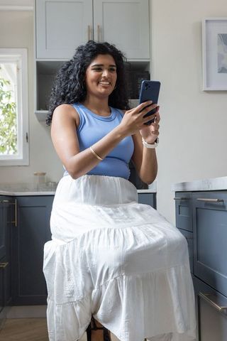 Indian woman smiling holding smartphone on kitchen stool in modern blue interior