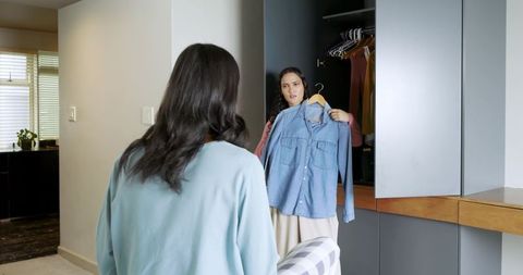 Friends choosing fashionable denim shirt in contemporary bedroom