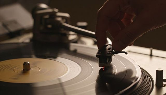 Lowering tonearm onto spinning vinyl record with warm ambient lighting for analog listening