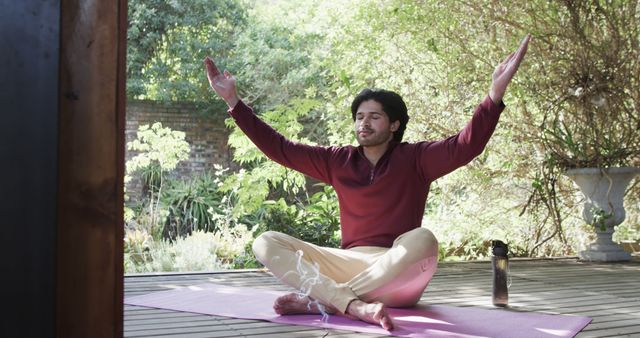 Biracial man practicing yoga meditation sitting on porch in garden. Summer, healthy lifestyle, wellbeing and free time concept, unaltered.