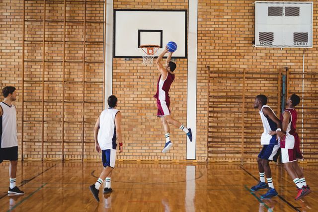 Basketball players are actively competing in an indoor court, showcasing teamwork and athleticism. This image is ideal for use in sports-related content, fitness promotions, teamwork and collaboration themes, and educational materials about basketball.
