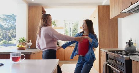 Mother and Daughter Joyfully Dancing in Sunlit Kitchen