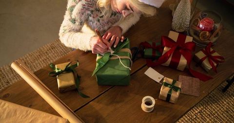 Woman wrapping holiday gifts on wooden table with ribbons, kraft paper and candlelight