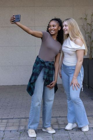 Smiling black and white friends taking selfie outdoors in casual street style