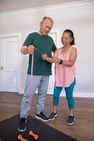 Senior asian couple measuring waist after home workout, tracking fitness progress