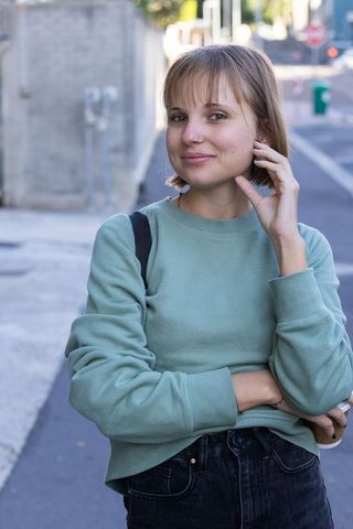 Young woman standing on city sidewalk wearing mint sweatshirt and backpack, smiling