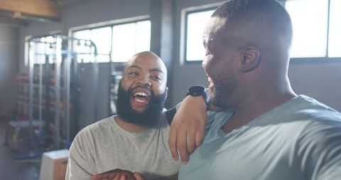 Two african men laughing together in gym showing friendship and workout motivation