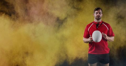 Confident Rugby Player Holding Ball Against Colorful Smoke Backdrop
