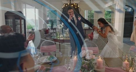 Bride leaning and laughing while holding groom's hand at intimate home reception with candles and ro