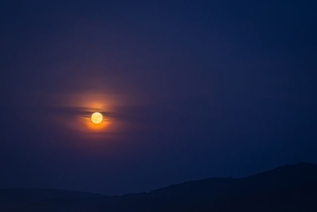 A full moon is shining brightly in the night sky over a mountainous landscape. This scene is tranquil and serene, with the detashaed glow of moonlight casting a celestial ambience. Ideal for backgrounds on relaxation or meditation apps, night sky event promotions, or nature photography galleries focusing on nocturnal landscapes.