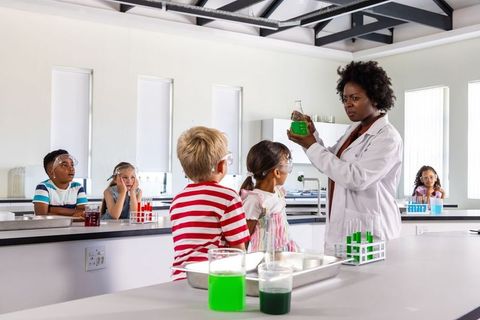 Stem teacher conducting colorful chemistry demonstration with elementary students in lab