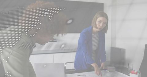 Pointing woman in blue blazer leaning over blueprint collaborating on architectural plan