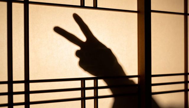 Hand shadow showing peace sign on shoji screen with warm backlight and wood lattice