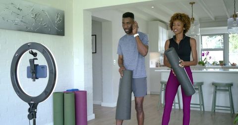 African american couple filming home fitness routine with yoga mats and ring light