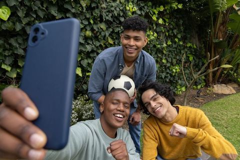 Teen friends taking selfie in backyard with soccer ball enjoying casual outdoor hangout