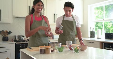 African American couple cooking and seasoning meal on marble kitchen island, smiling