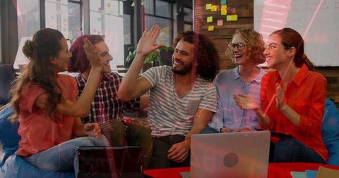 Startup team high-fiving in casual coworking lounge celebrating creative success